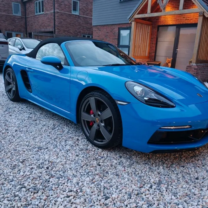 Blue Porsche 718 Boxster on a gravel driveway