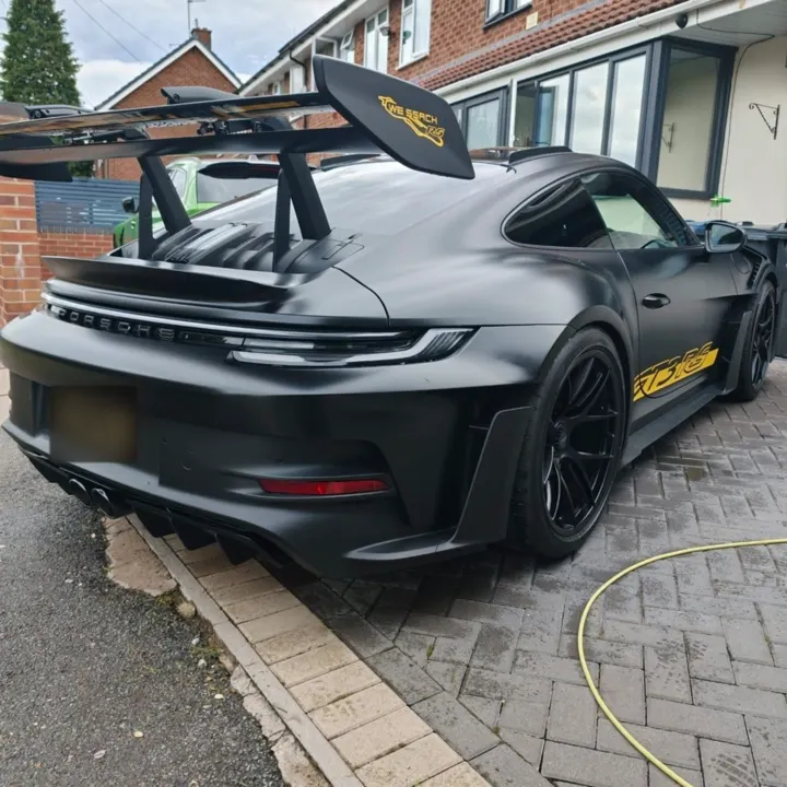 Satin black Porsche 911 GT3 RS with a large rear wing on a block-paved driveway