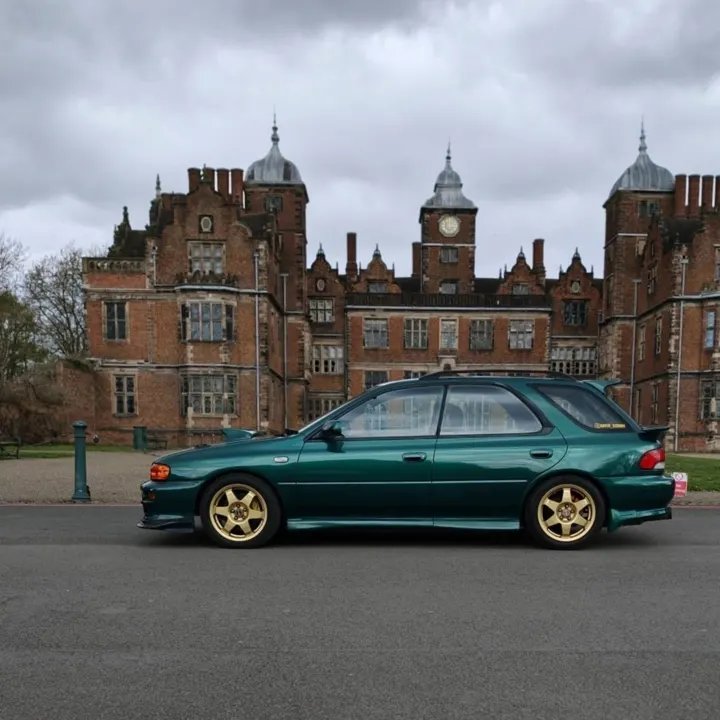 Green Subaru Impreza estate with gold wheels in front of a historic red-brick hall