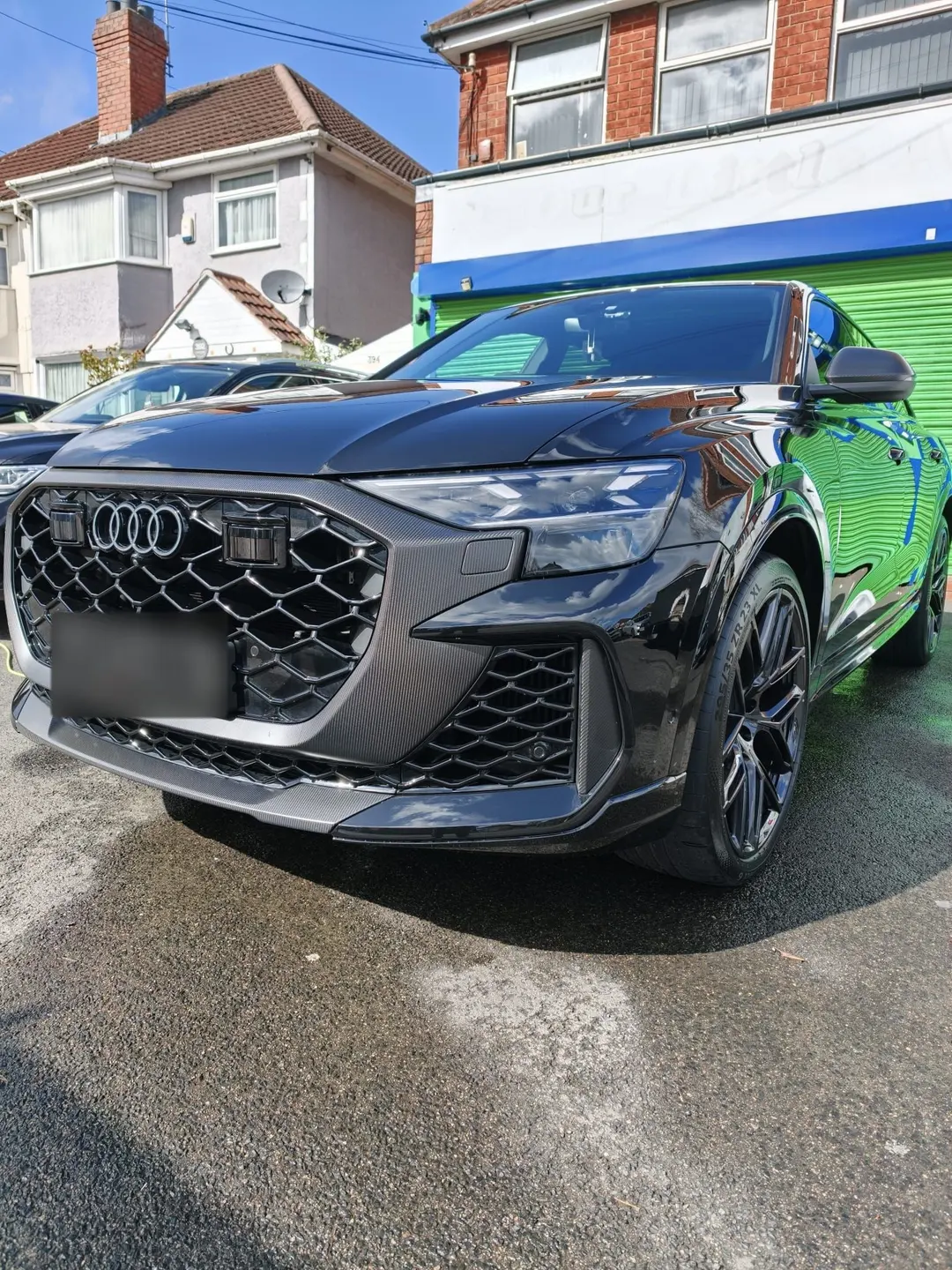 Black Audi RS Q8 with a carbon front grille, parked on a wet street