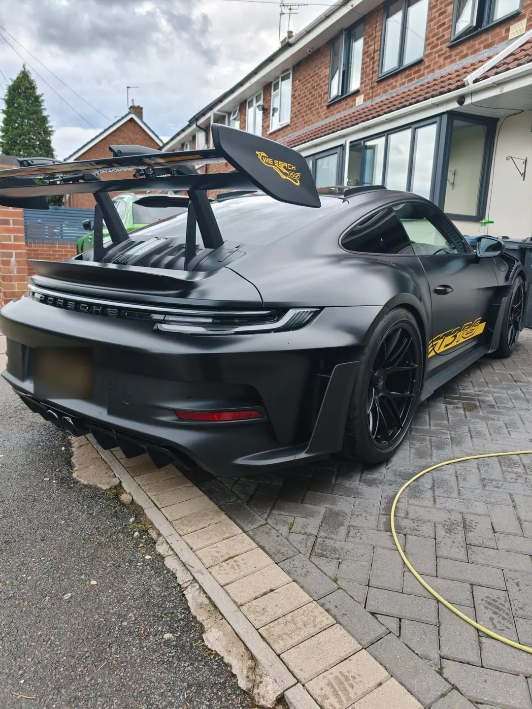 Satin black Porsche 911 GT3 RS with a large rear wing on a block-paved drive